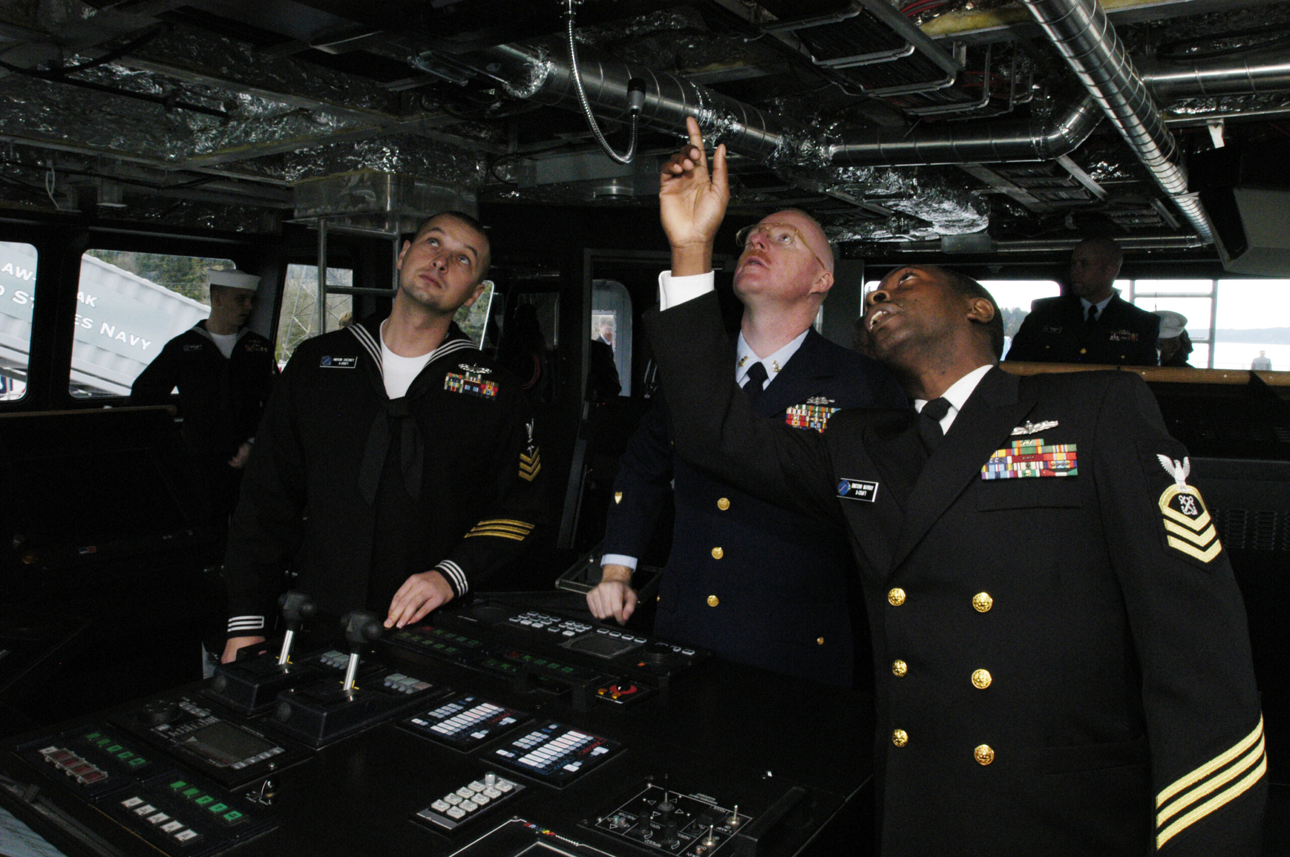Crew at a ship bridge console checking helm navigation instruments and displays