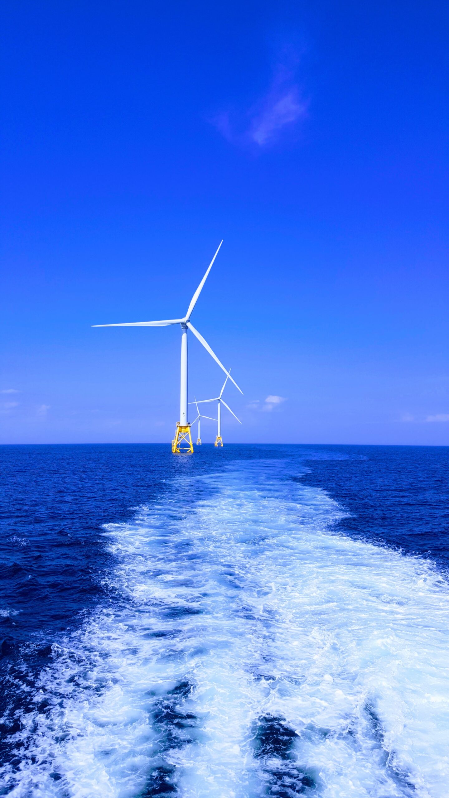 Tall offshore wind turbines rising from the sea under a clear sky; no ROV or drone is shown.